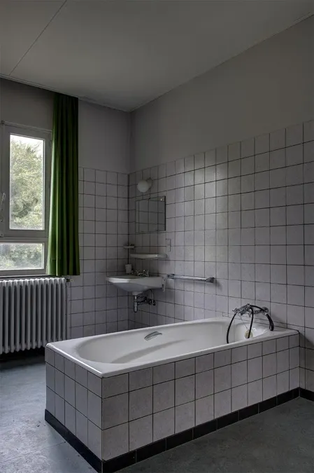 Baño alicatado con bañera blanca, lavabo pequeño y cortina verde.
