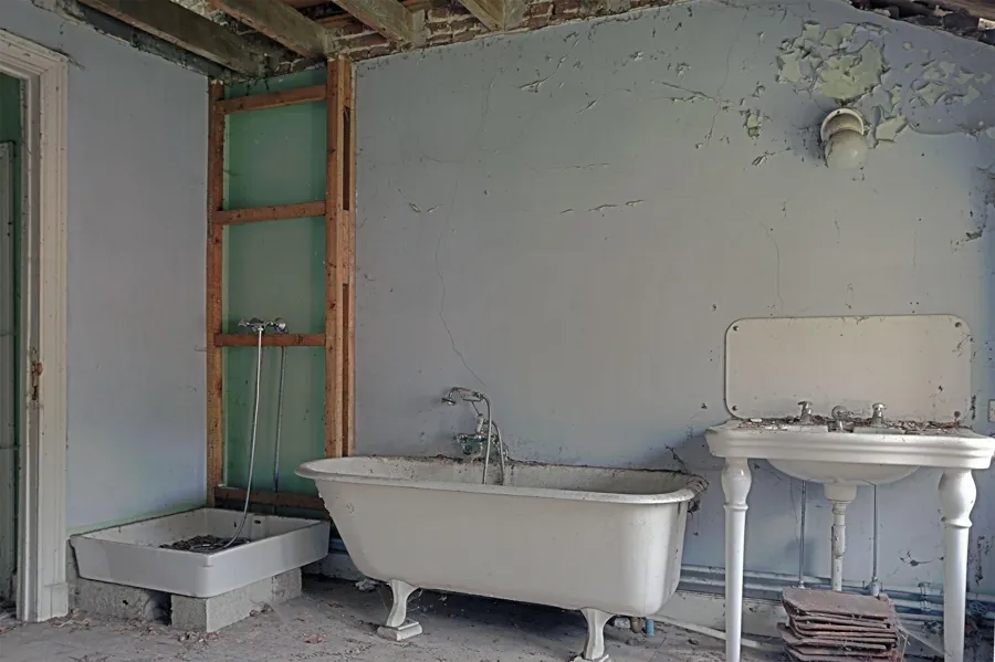 Baignoire sur pieds et lavabo dans une salle de bains abîmée