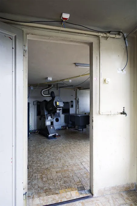 Vista por una puerta blanca abierta hacia un proyector en la sala técnica del fondo.