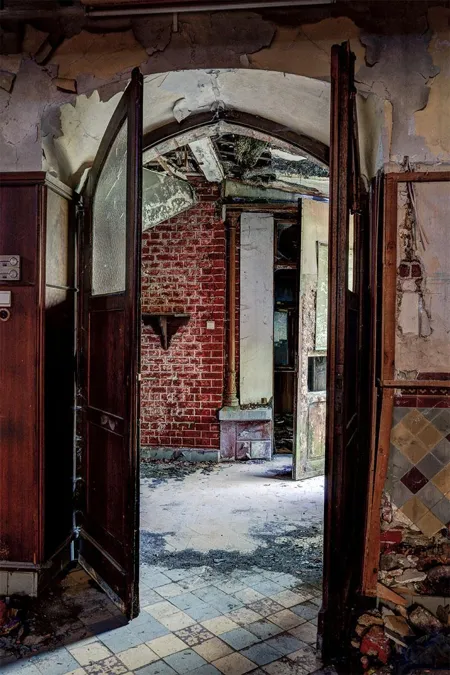 Open houten deuren tussen kapel en beschadigde bakstenen gang.