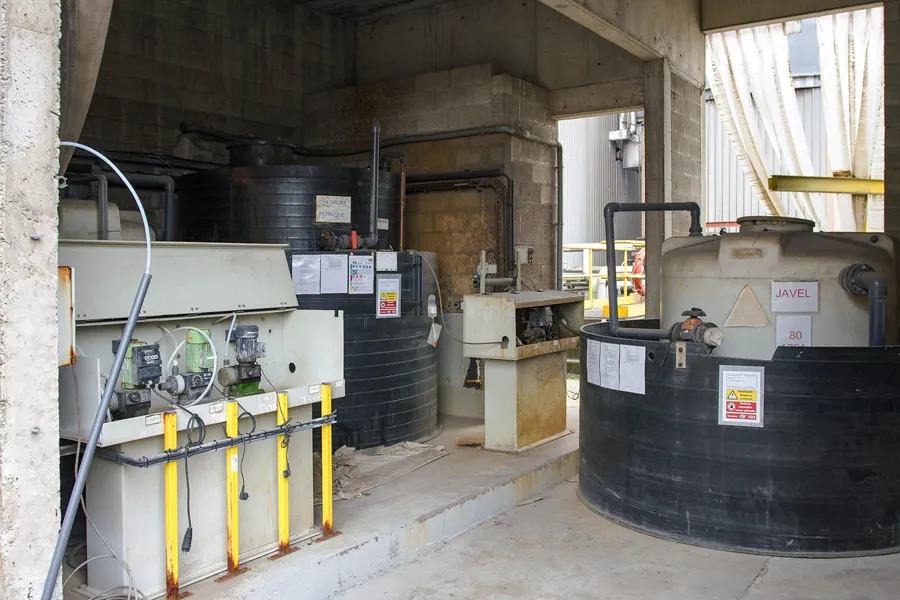 Large black storage tanks and dosing pumps in a bright factory room.