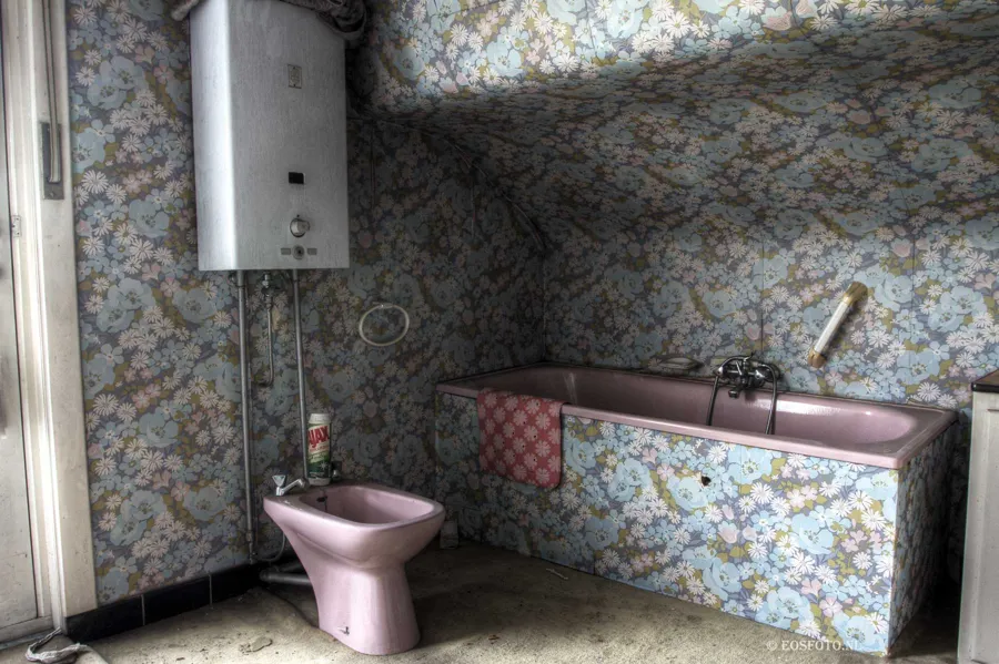 Rosa Badewanne und Bidet in einem Zimmer mit Blumentapete.