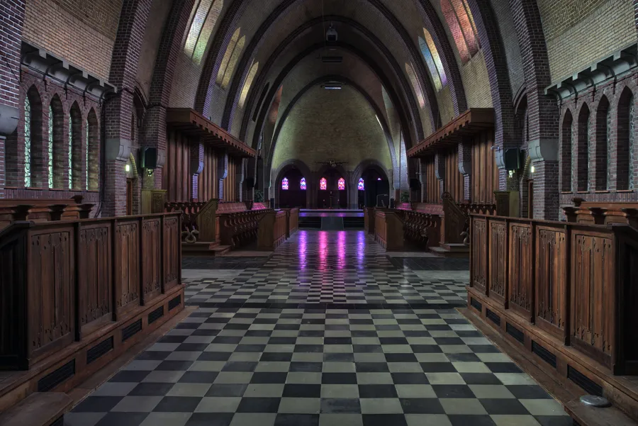 Interior amplio de capilla con sillería de madera y reflejos violetas en el suelo.