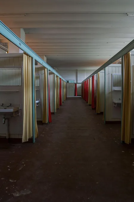 Lange gang tussen kleine afgeschermde ruimtes met gekleurde gordijnen.