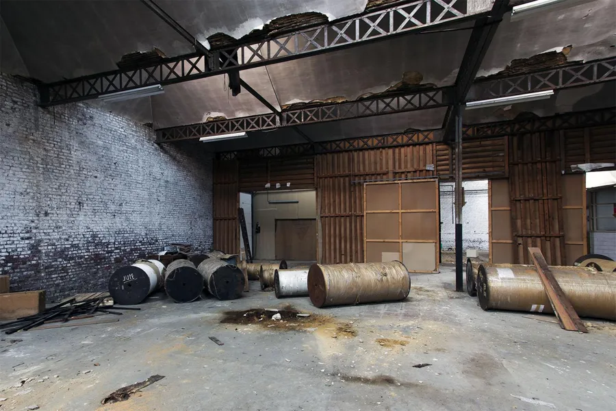 Grandes rodillos metálicos en el suelo de una sala industrial vacía.