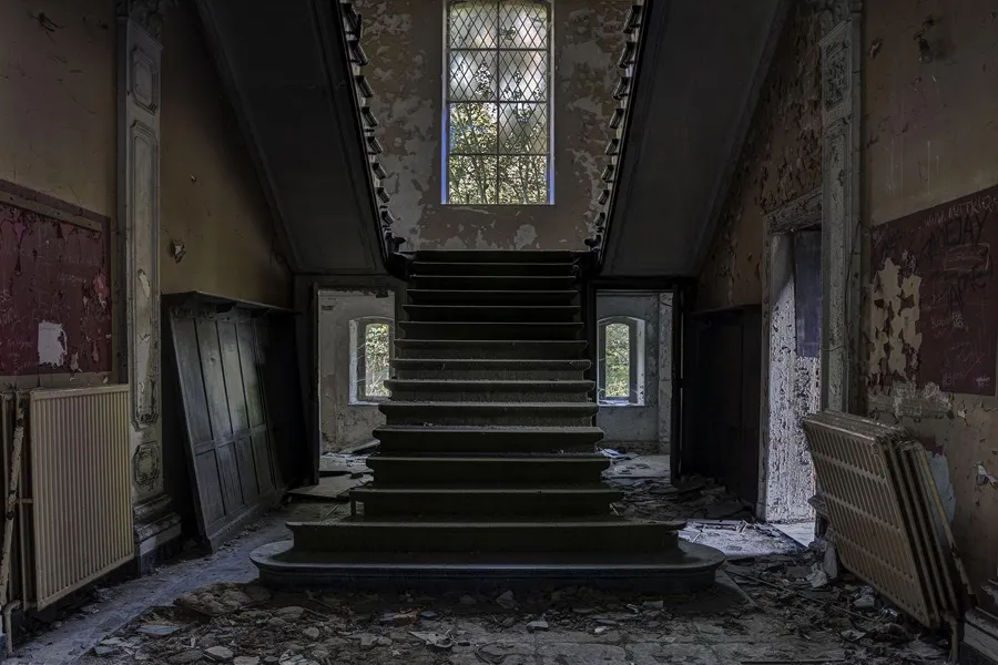 Large escalier entre murs abîmés et hautes fenêtres
