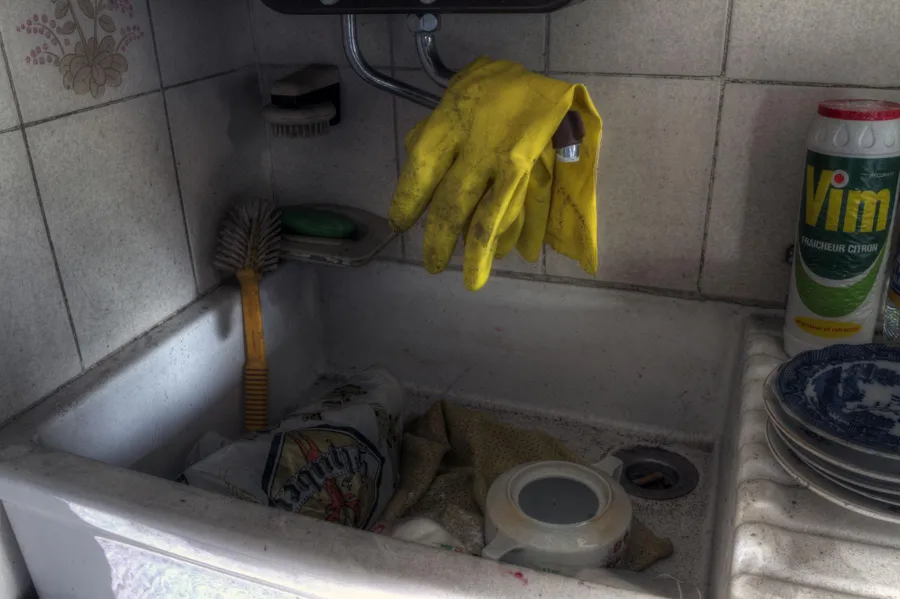 Schmutziges Spülbecken mit Verpackungen unter gelben Handschuhen.