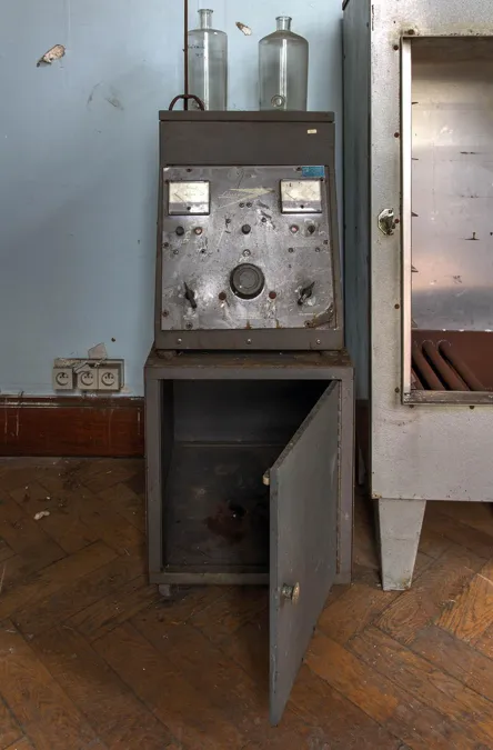 Old measuring apparatus in an open cabinet on a timber floor.
