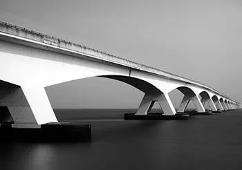 Vue en noir et blanc du pont de Zélande en diagonale sur l’eau lisse, avec des arches répétées jusqu’à l’horizon.