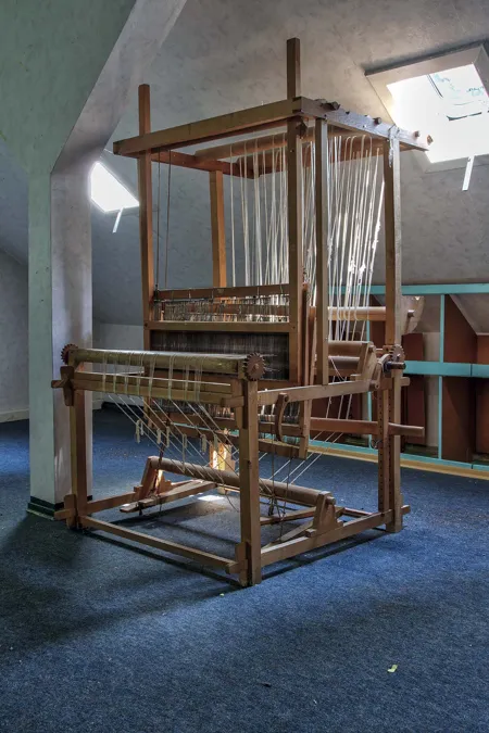 Houten weefgetouw op een blauwe vloer onder een schuin dak