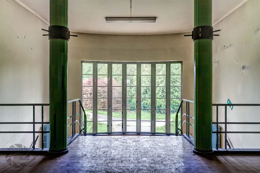 Glazed exterior door between green tiled columns and symmetrical stair railings.