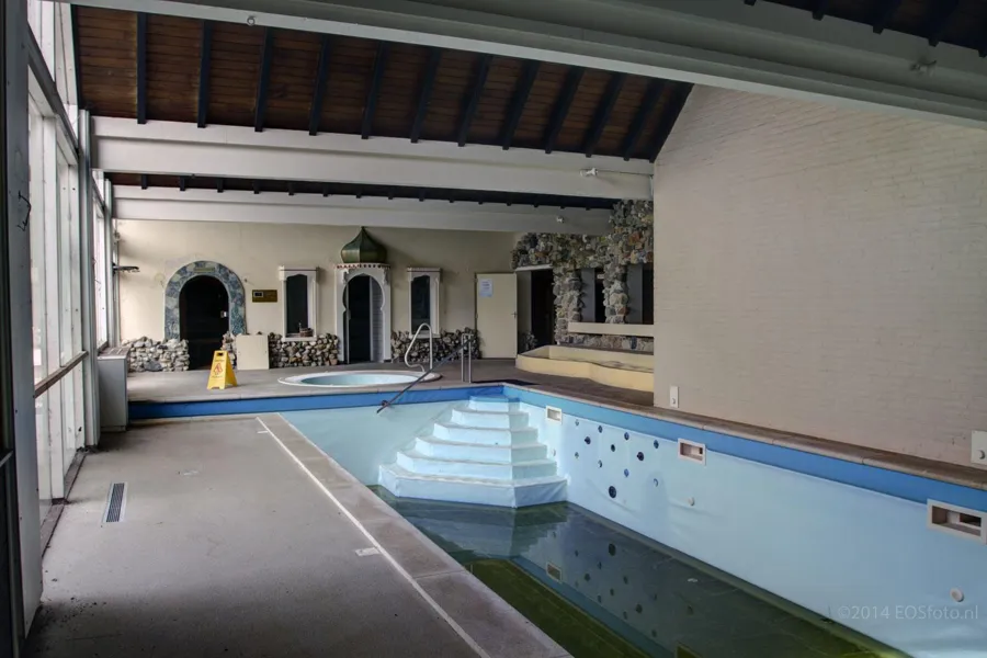 Piscina interior bajo vigas de madera con escalones al fondo.