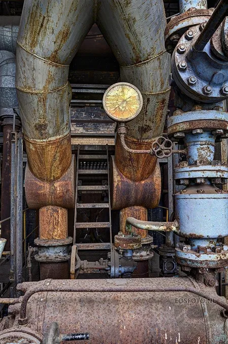 Yellow round gauge on a rusty pipe beside a blue flange.