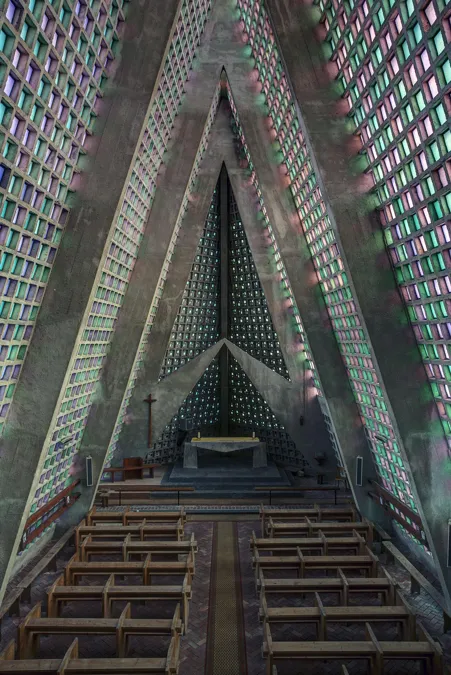 Vista elevada sobre bancos de madera hacia muro triangular del altar.