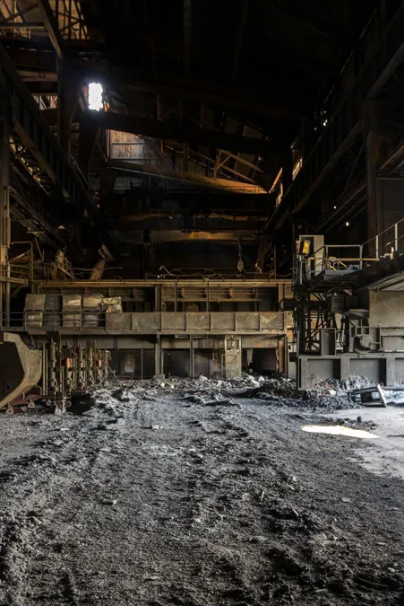 Donkere fabriekshal met ruwe materiaalhopen onder het stalen dak.