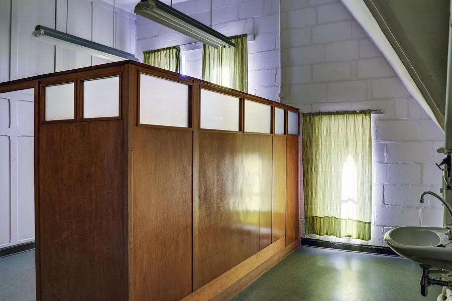 Houten scheidingswand met bovenlichten naast groene gordijnen en een wastafel.