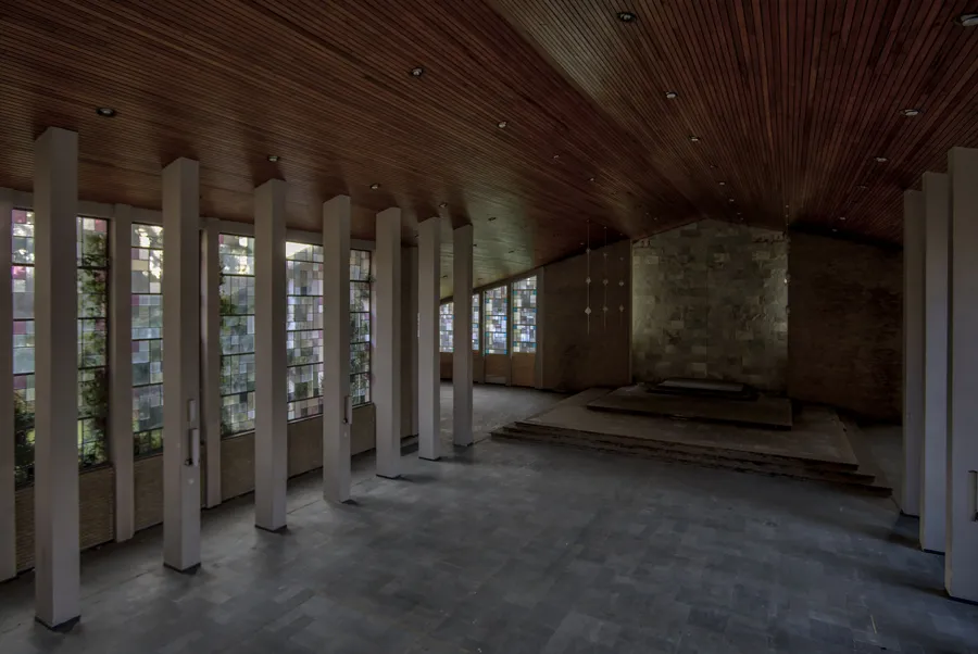 Sala larga con columnas blancas, cubierta de madera y vidrieras izquierdas.
