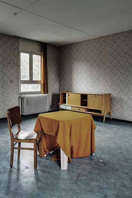 Habitación pequeña con mantel amarillo, silla de madera y mueble ante papel floral.