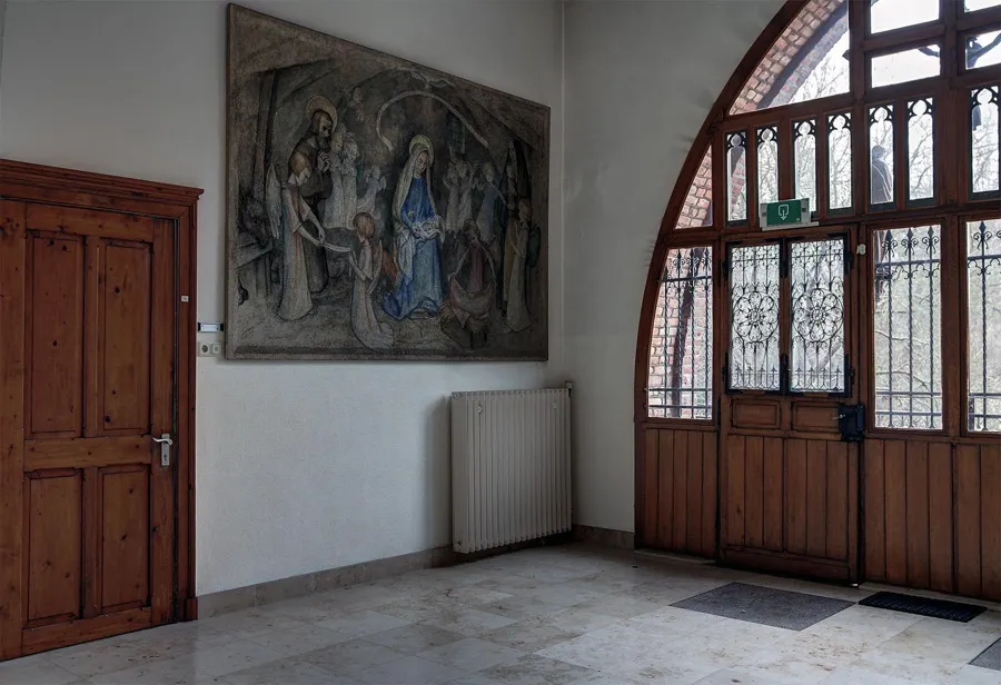 Houten buitendeuren met glas-in-lood naast een groot religieus reliëf aan de wand.