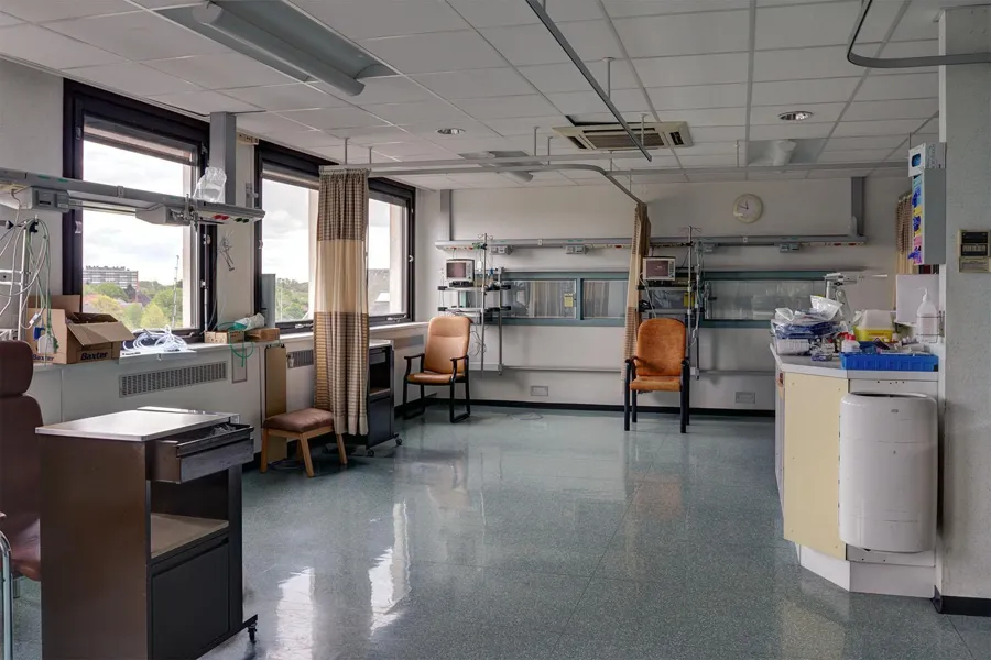 Disused care room with chairs, curtains and equipment along the walls.