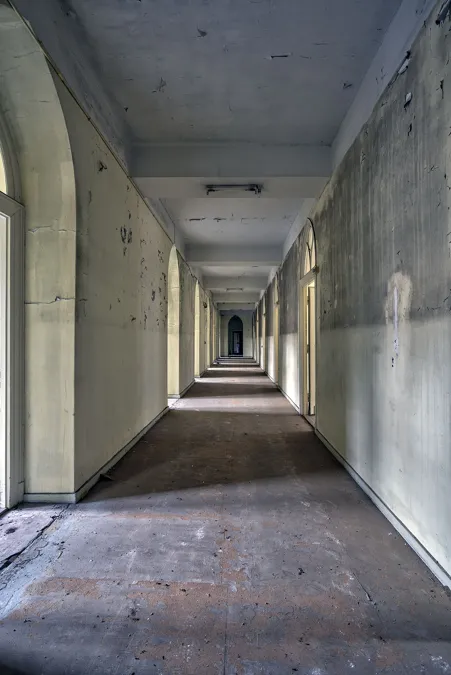 Pasillo largo recto con ventanas arqueadas a la izquierda y puerta oscura al fondo.