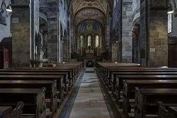 Mittelgang der Abteikirche Rolduc mit Holzbänken zwischen mächtigen Steinsäulen unter einem bemalten Gewölbe.