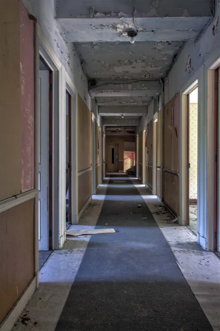 Long corridor with open room doors and a peeling ceiling.
