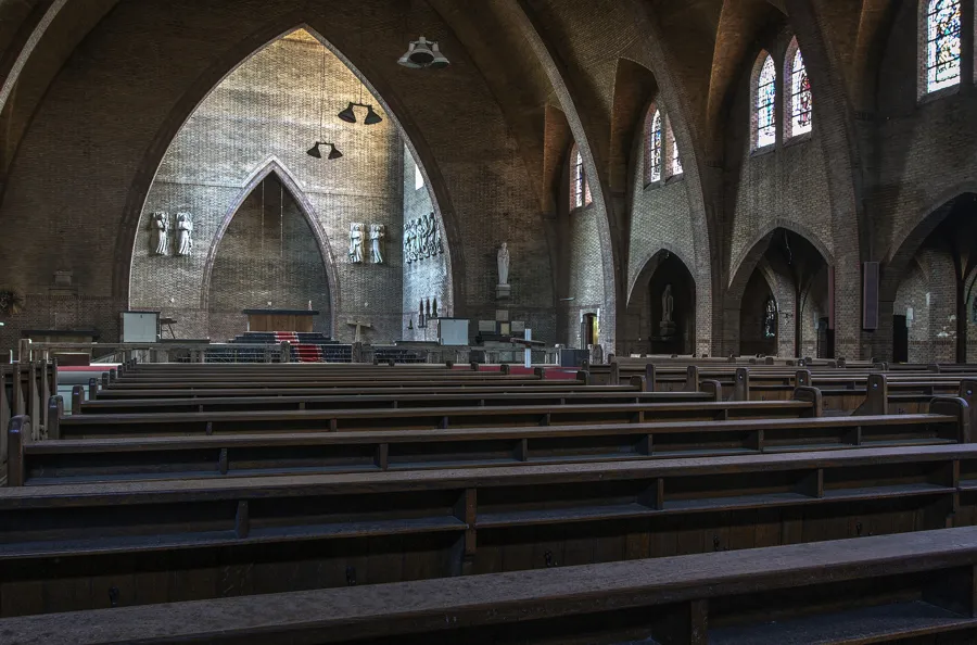 Breiter Kirchenraum mit leeren Bänken, Backsteinbögen und Hängelampen.