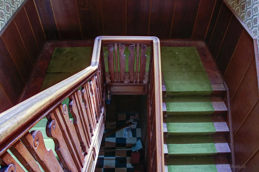 Escalera de madera con alfombra verde y paredes revestidas de madera