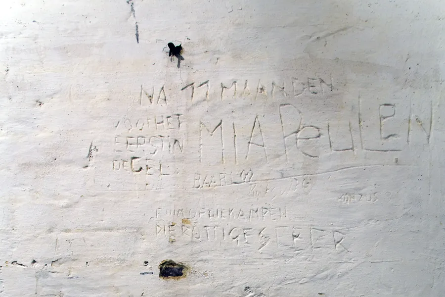 Letras arañadas en pared blanca deteriorada con pintura desconchada.