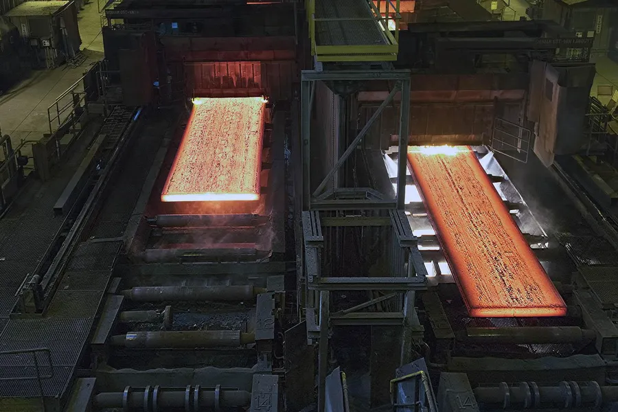 Vue oblique de deux plaques d’acier orange incandescent sur des rouleaux distincts.