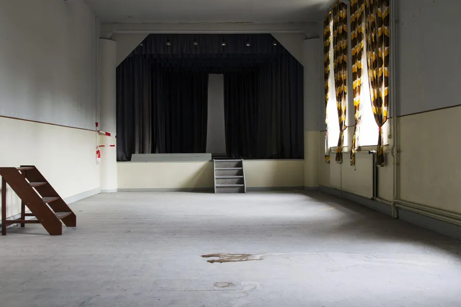 Lege zaal met podium, donkere gordijnen en een los houten trapje.