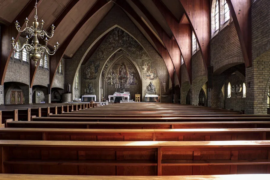 Side view across polished wooden pews towards the painted chancel, with a chandelier at upper left.