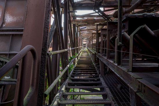 Schmale Metalltreppe zwischen rostigen Fabrikkonstruktionen
