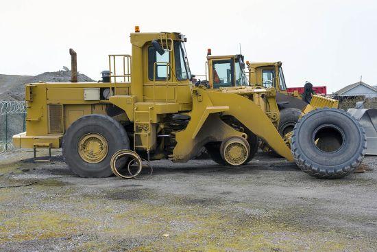 Two yellow wheel loaders and a detached wheel on the factory grounds