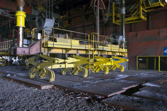 Yellow machine with several grippers above railway tracks inside the hall