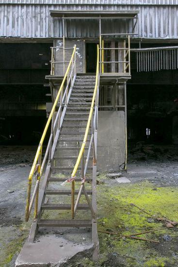 Narrow exterior stairs with yellow handrails leading to a factory door