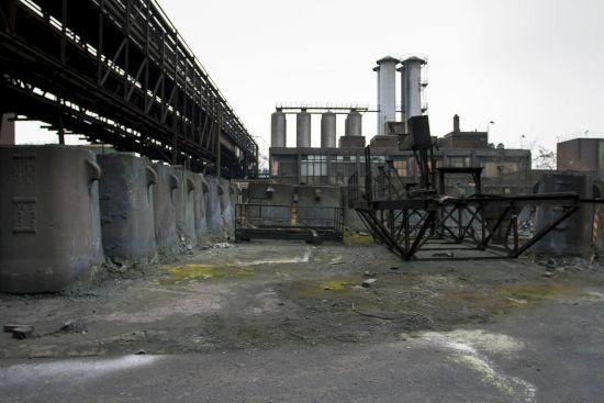 Pipes on a steel bridge leading to buildings with tall chimneys