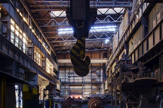 Dark crane hook hanging beneath an overhead crane in the tall factory hall