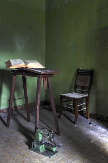 Libro abierto sobre mesa alta junto a una silla ante una pared verde