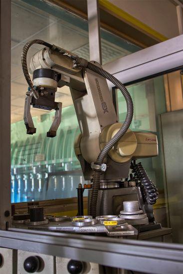 Grauer Maschinenarm über einer Arbeitsfläche mit Laborgeräten