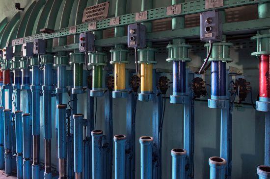 Lange Reihe blauer Röhren und farbiger Zylinder unter einer Metallschiene